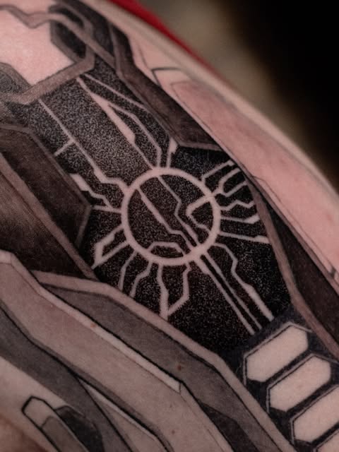 Close-up of a black and grey geometric tattoo with a circular symbol and radiating lines.