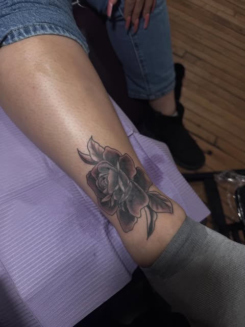 Black and grey rose tattoo with leaves on the lower leg.
