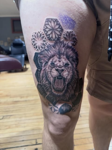 Black and grey roaring lion tattoo with circular ornamental motifs on the thigh.