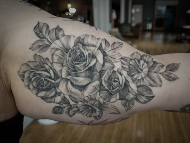 Black and grey floral tattoo with large roses, small blossoms, and leaves.