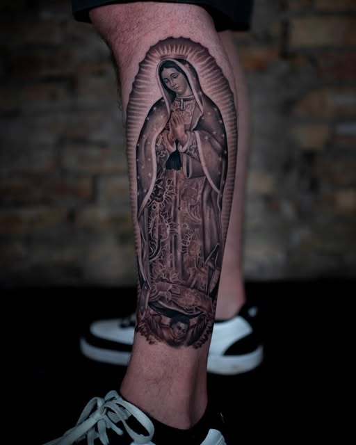 Black and grey Virgin Mary tattoo framed by radiant lines on a lower leg.